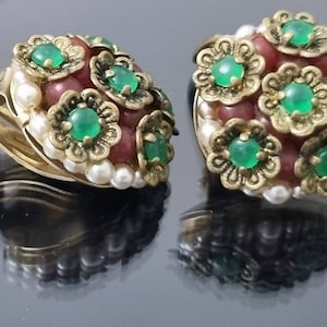 Peut inclure: Une paire de boucles d'oreilles clips dorées avec des accents de fleurs vertes et rouges. Les boucles d'oreilles sont décorées de petites perles blanches.