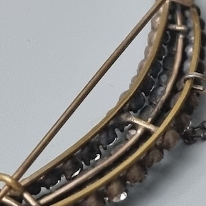 May include: A crescent moon shaped brooch with a gold tone metal setting and a row of clear rhinestones around the edge.