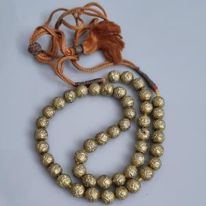 May include: A gold beaded necklace with a brown tassel. The beads are round and have a textured surface.