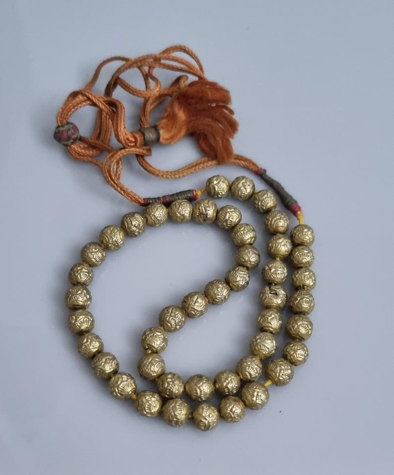 May include: A gold beaded necklace with a brown tassel. The beads are round and have a textured surface.