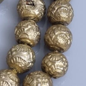 May include: A strand of gold-colored beads with intricate designs. The beads are round and have a textured surface.