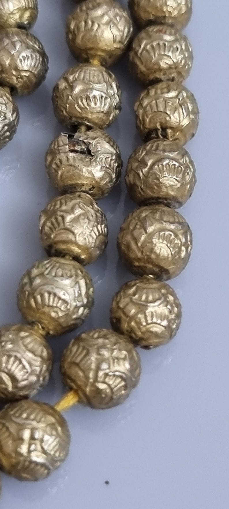 May include: A strand of gold-colored beads with intricate designs. The beads are round and have a textured surface.