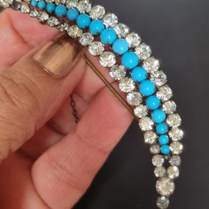 May include: A vintage brooch with a crescent shape design featuring a row of turquoise blue stones surrounded by clear rhinestones.