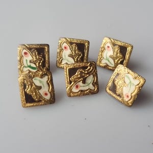 May include: A collection of six square vintage buttons. Each button features a gold-colored frame with a dark brown center. The center design includes a white and green floral motif with red accents. The buttons are likely for sewing or crafts.