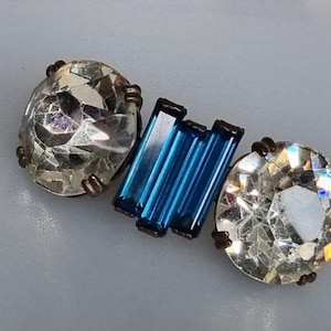 May include: A vintage brooch with three clear faceted glass stones and a blue glass bar in the center.