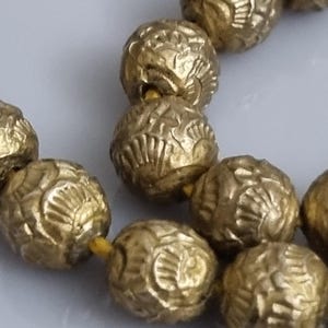 May include: A strand of gold-colored beads with a textured surface. The beads are strung together with a thin yellow thread.