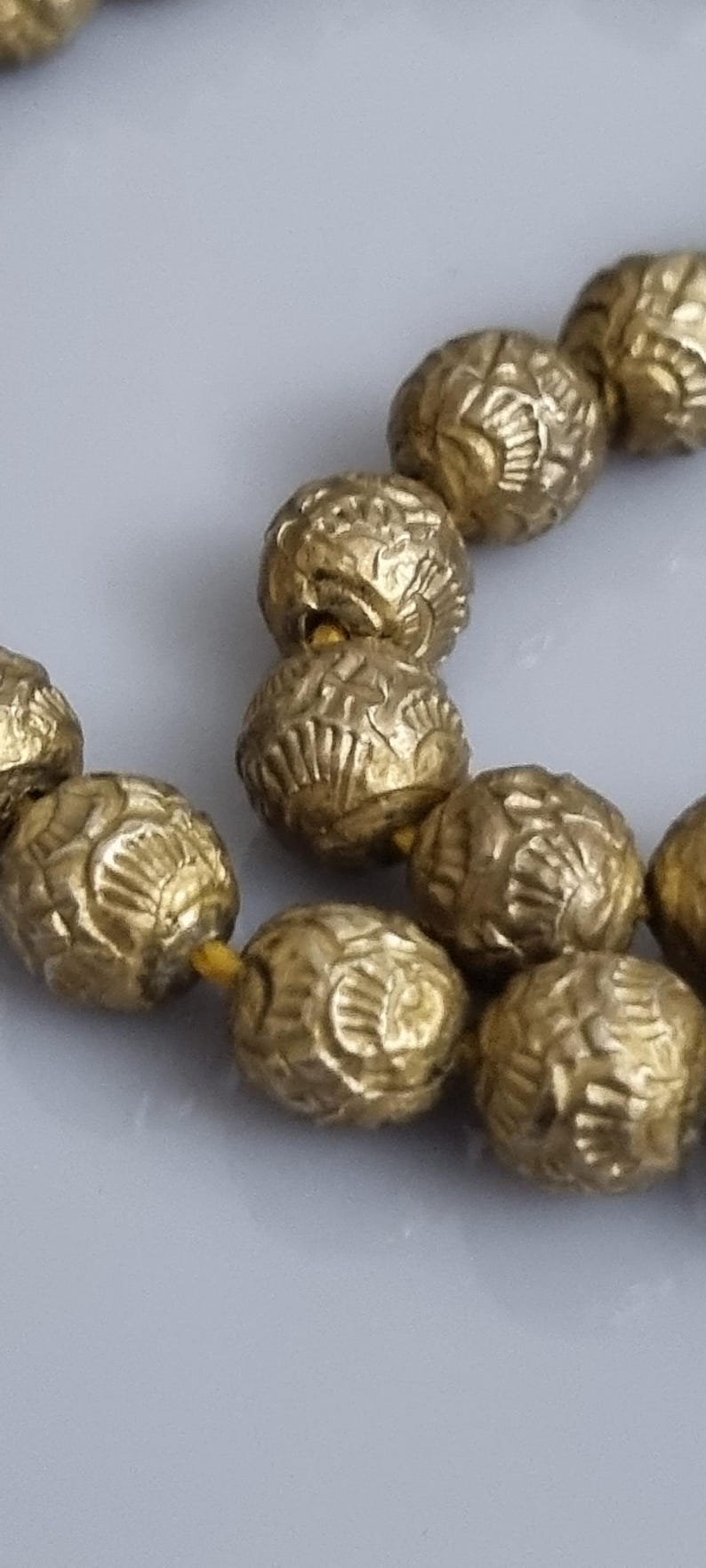 May include: A strand of gold-colored beads with a textured surface. The beads are strung together with a thin yellow thread.