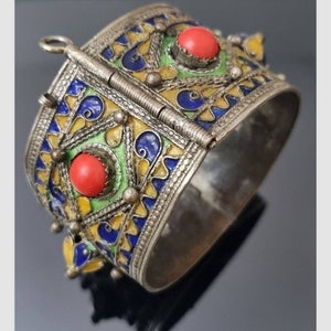 May include: A silver bracelet with intricate enamel work in blue, green, and yellow. The bracelet has two red coral stones and a hinged clasp.