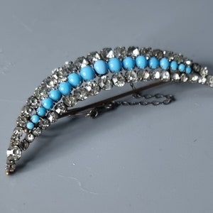 May include: A crescent-shaped brooch with a row of turquoise blue stones set in silver, surrounded by clear rhinestones.