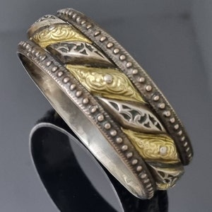 Puede incluir: Un anillo de plata y oro con diseños intrincados. El anillo tiene una banda ancha con un patrón retorcido y un borde decorativo.