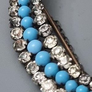 May include: A crescent-shaped brooch with a silver chain and blue and clear glass beads.