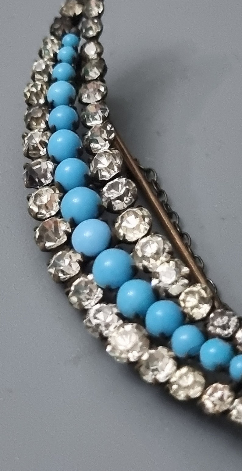May include: A crescent-shaped brooch with a silver chain and blue and clear glass beads.