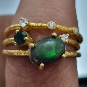 Op de afbeelding: Een gouden ring met een zwarte opaal en groene smaragden. De ring is bezet met kleine diamanten.
