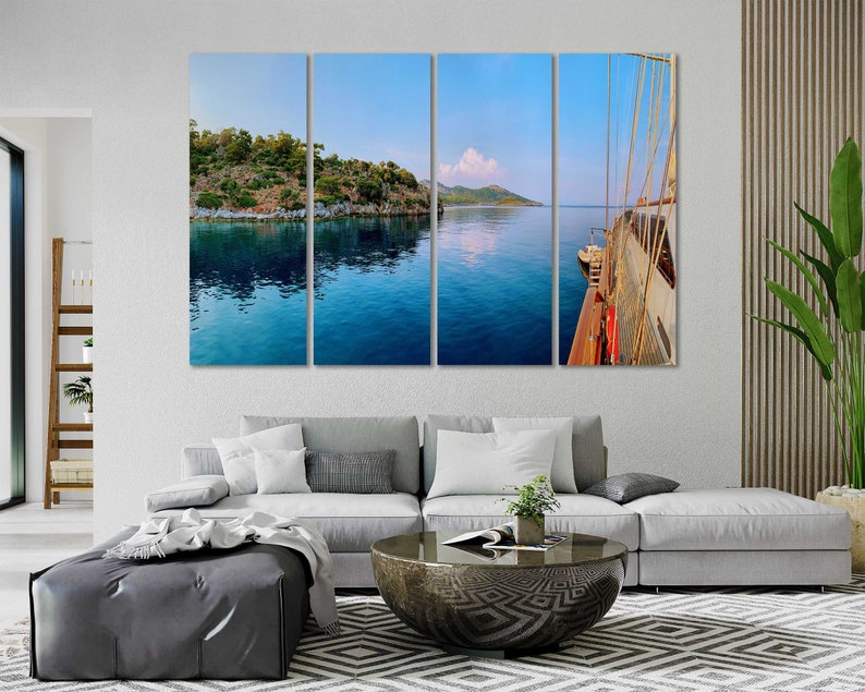 May include: A panoramic view of a blue body of water with a green island in the distance. A white sailboat is docked on the right side of the image.