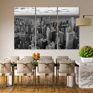 May include: A black and white photo of a city skyline with tall buildings. The photo is split into three panels and is hanging on a wall above a dining table with chairs.