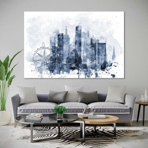 May include: A watercolor painting of a city skyline in shades of blue. The skyline includes tall buildings, a Ferris wheel, and a church steeple. The painting has a white background with splatters of blue paint.