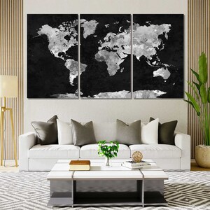 May include: A black and white world map print with a distressed, watercolour effect. The map is split into three panels, each featuring a portion of the world. The map is displayed on a white wall above a white sofa with cushions and a coffee table.