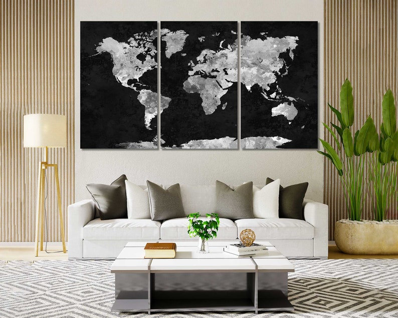 May include: A black and white world map print with a distressed, watercolour effect. The map is split into three panels, each featuring a portion of the world. The map is displayed on a white wall above a white sofa with cushions and a coffee table.