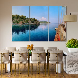 May include: A three-panel canvas print depicting a view of a blue body of water with a green island in the distance. The right panel shows a wooden boat with white sails.