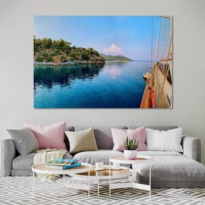 May include: A view from the deck of a sailboat, looking out at a calm blue sea with a small island in the distance. The sky is a light blue with a few white clouds.