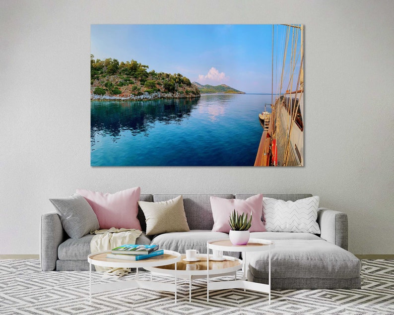 May include: A view from the deck of a sailboat, looking out at a calm blue sea with a small island in the distance. The sky is a light blue with a few white clouds.