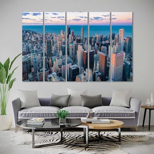 May include: A multi-panel canvas print featuring an aerial view of a city skyline at sunset. The city is filled with tall buildings and skyscrapers, with a river or lake in the distance. The sky is a mix of orange, pink, and purple hues.