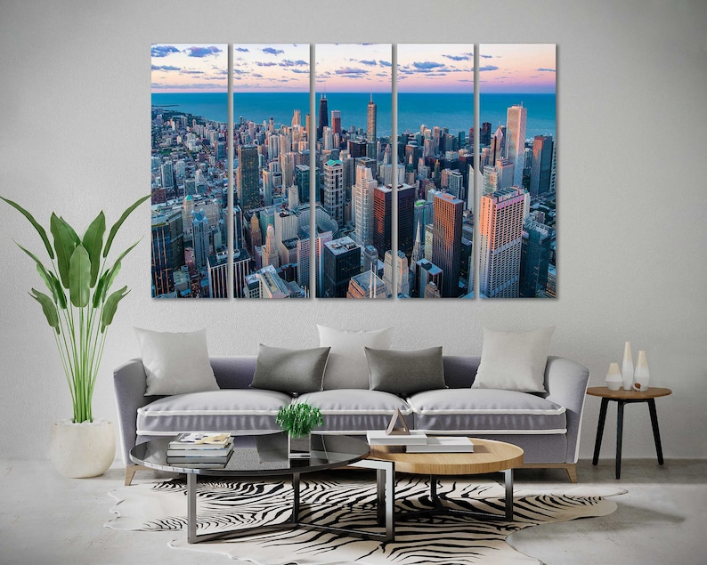 May include: A multi-panel canvas print featuring an aerial view of a city skyline at sunset. The city is filled with tall buildings and skyscrapers, with a river or lake in the distance. The sky is a mix of orange, pink, and purple hues.