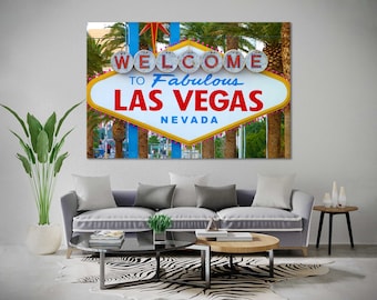 May include: A vintage-style sign with the words "Welcome to Fabulous Las Vegas, Nevada" in red, blue, and yellow letters. The sign is surrounded by palm trees and a blue sky.
