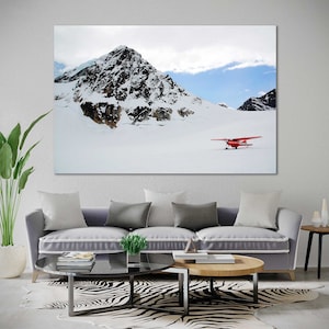 May include: A red airplane sits on a snowy mountaintop with a large, snow-covered peak in the background.
