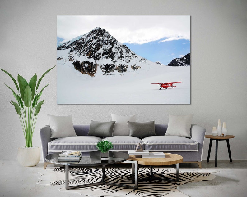 May include: A red airplane sits on a snowy mountaintop with a large, snow-covered peak in the background.