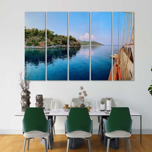 May include: A multi-panel canvas print depicting a scenic view of a turquoise blue body of water with a small island in the distance. The water reflects the sky, which is a light blue with a few white clouds. The right panel shows a wooden boat with white sails.