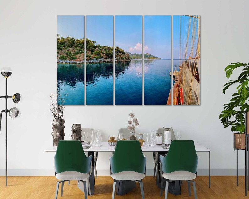 May include: A multi-panel canvas print depicting a scenic view of a turquoise blue body of water with a small island in the distance. The water reflects the sky, which is a light blue with a few white clouds. The right panel shows a wooden boat with white sails.
