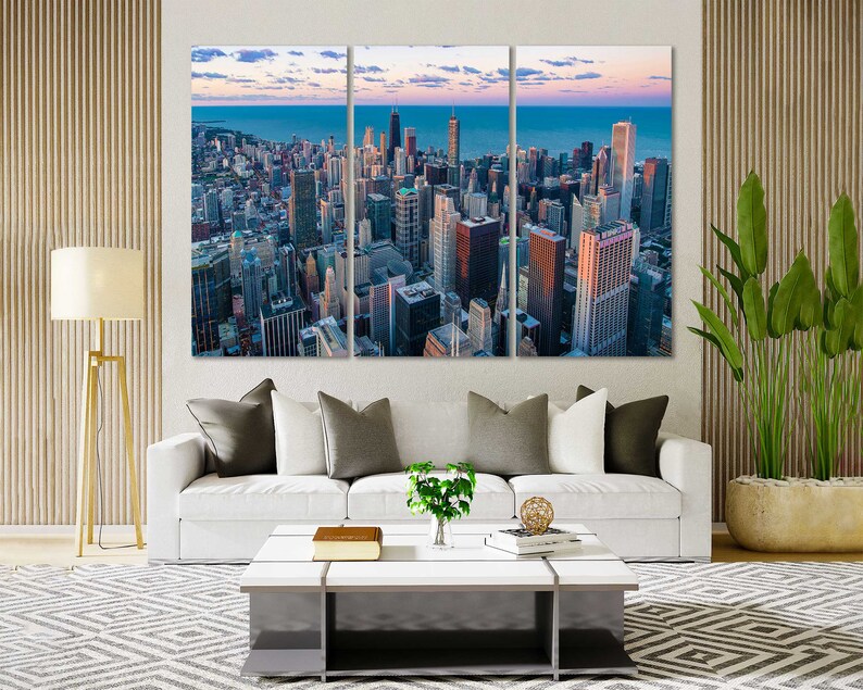 May include: A panoramic view of a city skyline with tall buildings and a body of water in the background. The buildings are mostly gray and brown, with some blue accents. The sky is a light blue with some clouds.