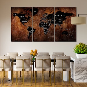 May include: A three-piece set of black and white world maps with a distressed brown background. The maps are framed and hung on a beige wall above a dining table with gold chairs.