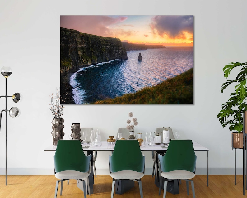 Puede incluir: Una fotograf&iacute;a panor&aacute;mica de los Acantilados de Moher en Irlanda, con un cielo de puesta de sol dram&aacute;tico y un afloramiento rocoso en el oc&eacute;ano. Los acantilados son verdes y marrones, y el agua es de un azul profundo.