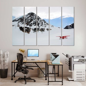 May include: A multi-panel canvas print of a snowy mountain landscape with a red airplane flying over the snow. The print is hanging on a white wall above a desk with a computer, chair, and printer.