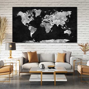 May include: A living room interior with a white brick wall, a grey sofa with two tan cushions, a coffee table with a book and a bowl, a black and white world map print hanging on the wall, and two tan armchairs with gold frames.