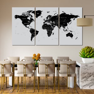 May include: A three-panel world map art piece in black and white, with country names labeled. The artwork is displayed above a dining table with gold-framed chairs. A lamp and a succulent plant in a white pot are also visible.