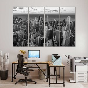 May include: A black and white photo of a city skyline, split into three panels. The photo is hanging on a white wall above a desk with a black office chair, a computer, and a printer.