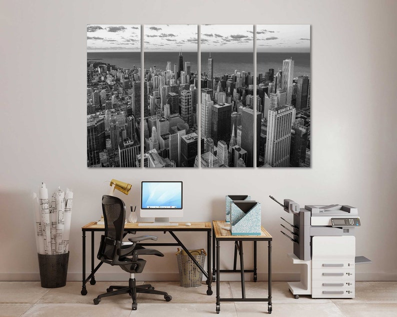 May include: A black and white photo of a city skyline, split into three panels. The photo is hanging on a white wall above a desk with a black office chair, a computer, and a printer.
