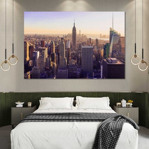 May include: A photograph of the New York City skyline at sunset. The image is printed on canvas and framed in a modern, black frame. The canvas is stretched over a wooden frame and has a textured surface. The frame is made of wood and has a black finish.
