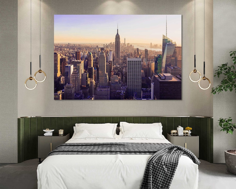May include: A photograph of the New York City skyline at sunset. The image is printed on canvas and framed in a modern, black frame. The canvas is stretched over a wooden frame and has a textured surface. The frame is made of wood and has a black finish.