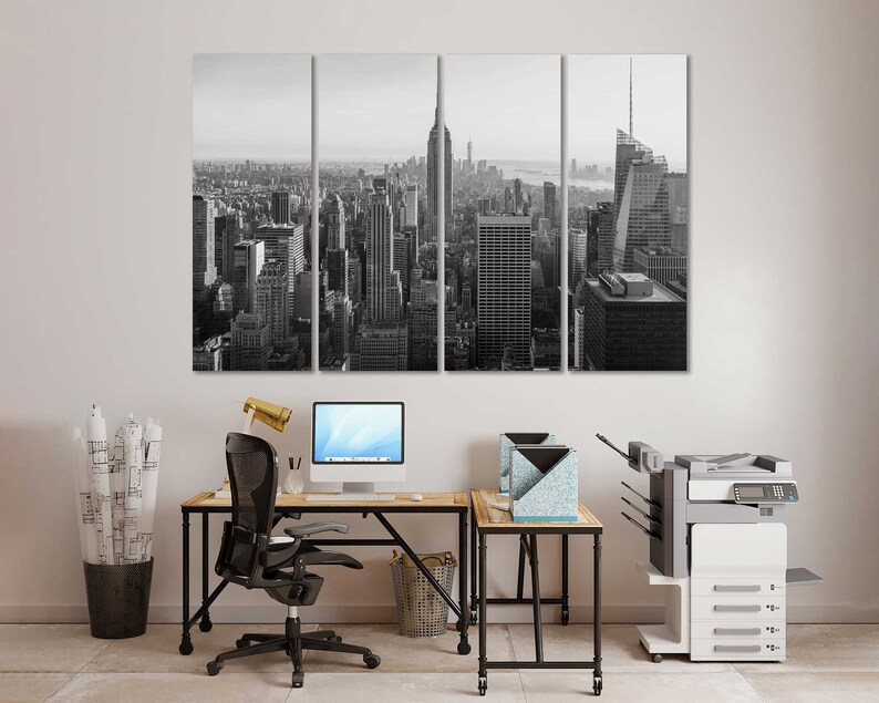 May include: A black and white photo of a city skyline, split into three panels. The photo is hanging on a white wall above a desk with a black office chair, a computer, and a printer.