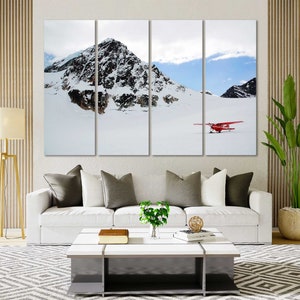 May include: A red airplane flying over a snowy mountain range. The plane is in the foreground, and the mountains are in the background. The sky is blue and there are clouds in the sky.