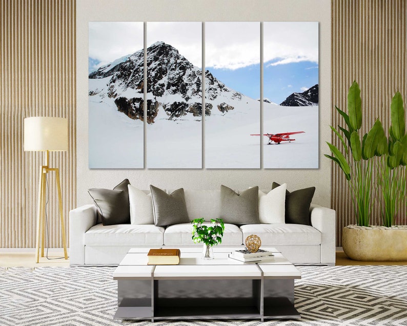 May include: A red airplane flying over a snowy mountain range. The plane is in the foreground, and the mountains are in the background. The sky is blue and there are clouds in the sky.