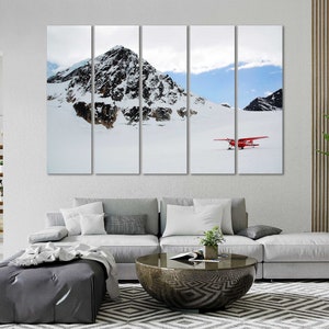 May include: A multi-panel canvas print featuring a snowy mountain landscape with a red airplane flying over a snow-covered field.