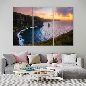 Puede incluir: Una vista panor&aacute;mica de los Acantilados de Moher en Irlanda al atardecer. Los acantilados son un hito natural dram&aacute;tico con una costa accidentada y un oc&eacute;ano azul profundo. El cielo es una mezcla vibrante de tonos rosados, naranjas y morados, creando un tel&oacute;n de fondo impresionante para los acantilados.
