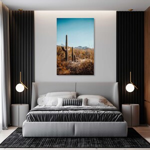 May include: A photograph of a desert landscape with tall cacti in the foreground. The sky is blue and the ground is covered in brown brush.