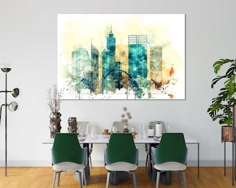 May include: A large canvas print featuring a watercolor-style cityscape. The artwork showcases a skyline with tall buildings in shades of teal, blue, and yellow. The print is displayed above a dining table with green chairs, creating a modern interior design.