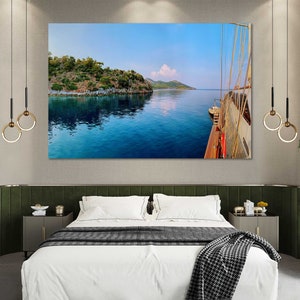 May include: A panoramic photograph of a blue body of water with a green island in the distance. The water is calm and reflects the sky. A wooden boat is docked on the right side of the image.